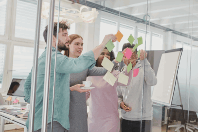 Gruppe von Menschen arbeitet an Glaswand mit Notizzetteln – Symbol für Gemeinschaft, Wachstum und persönliche Entwicklung im Rahmen von Kursen und Workshops zu Lebensthemen.